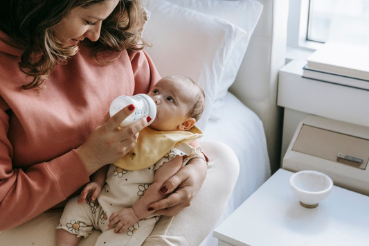 A mother feeds her baby with a bottle in a cozy bedroom setting